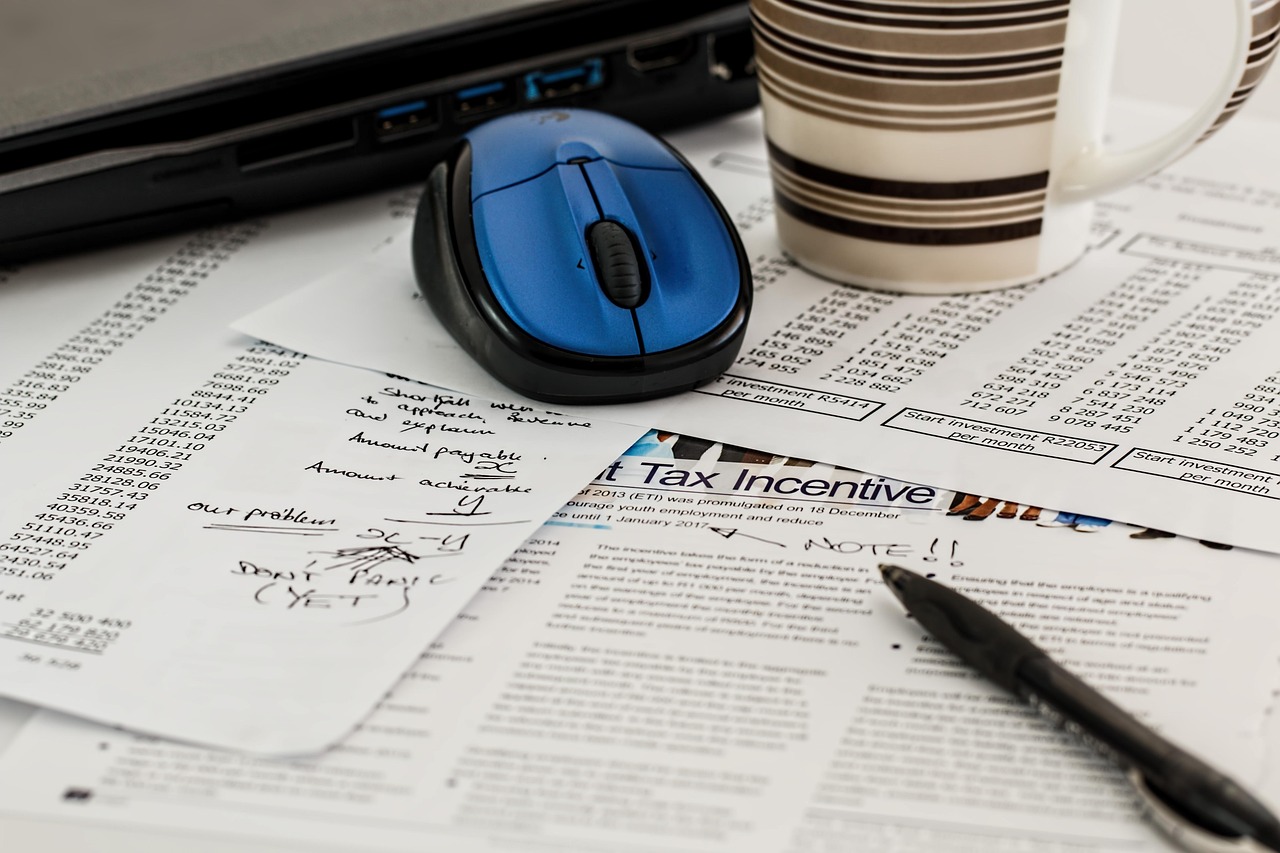 Journal ouvert sur un article intitulé Tax Incentive, avec une souris et un café