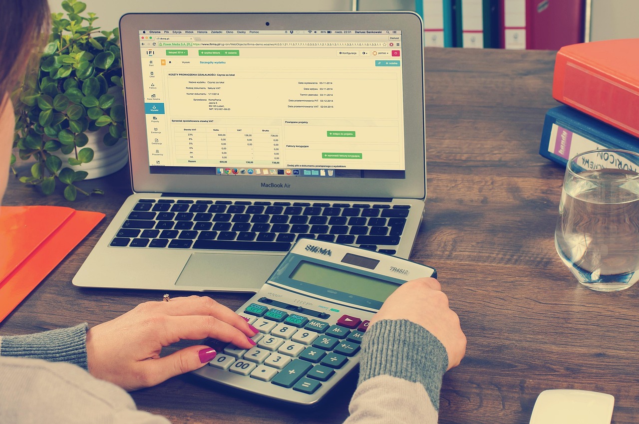 Personne utilisant une calculatrice devant un ordinateur portable affichant un tableau de bord financier