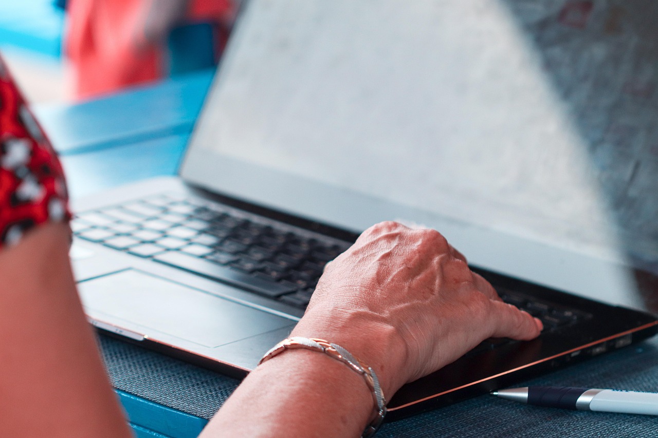 Main d'une personne senior tapant sur le clavier d'un ordinateur portable