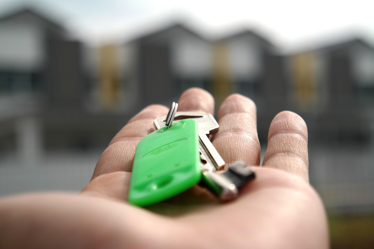 Main tenant un trousseau de clés vertes devant des maisons en arrière-plan